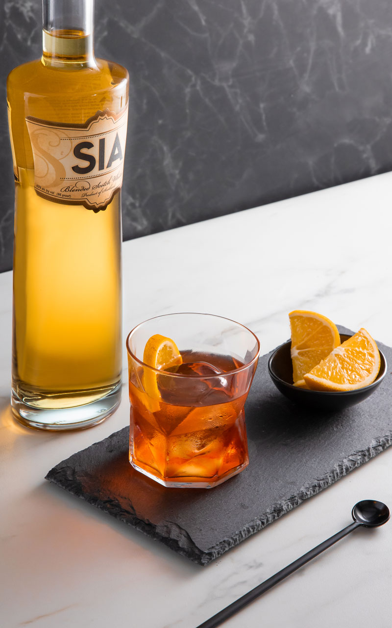 A bottle of SIA Blended Scotch Wisky behind a SIA Negroni cocktail