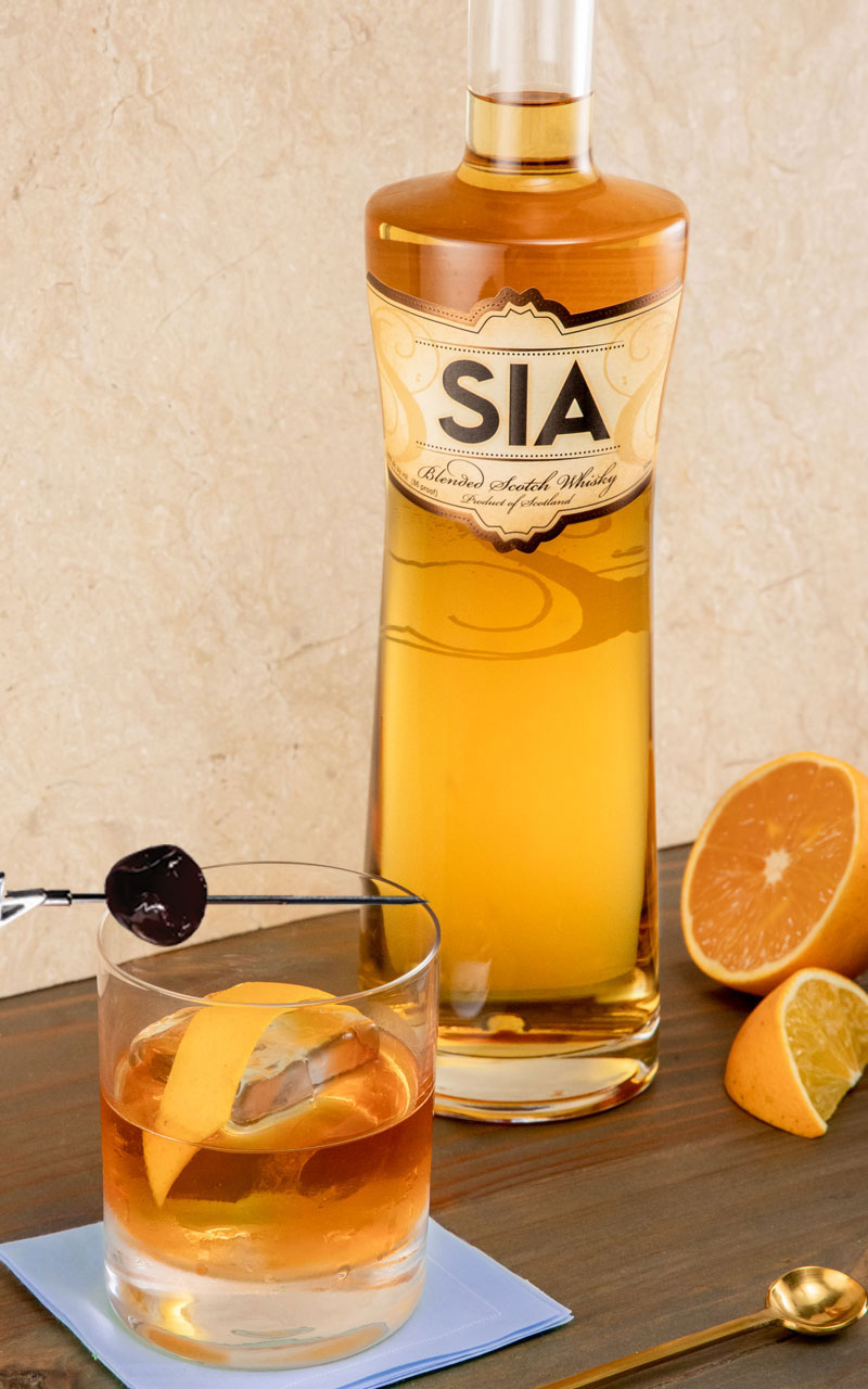 A bottle of SIA Blended Scotch Wisky behind a SIA Old Fashioned cocktail